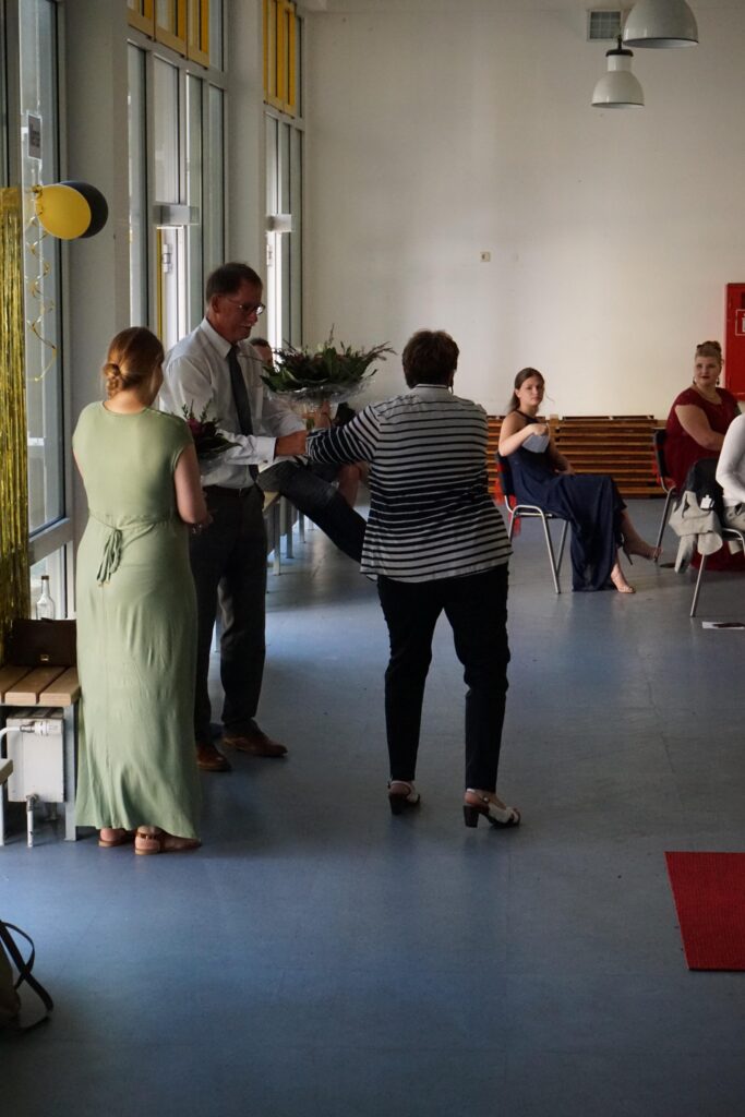Menschen in einem Raum, einige im Gespräch, andere sitzen auf Stühlen.