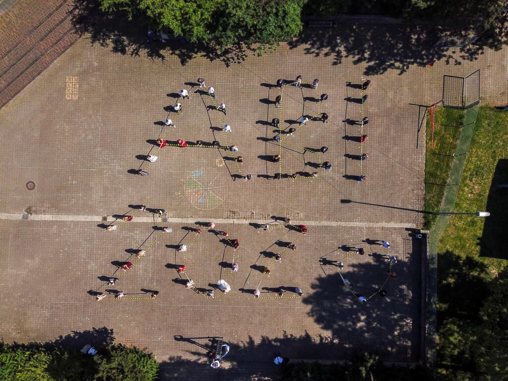 Schüler bilden mit ihrem Körper die Schriftzüge "ABI 2023" auf einem Platz.
