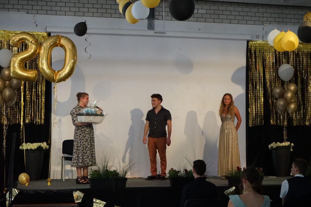 Drei Personen auf der Bühne, dekoriert mit Luftballons und goldenen Zahlen.