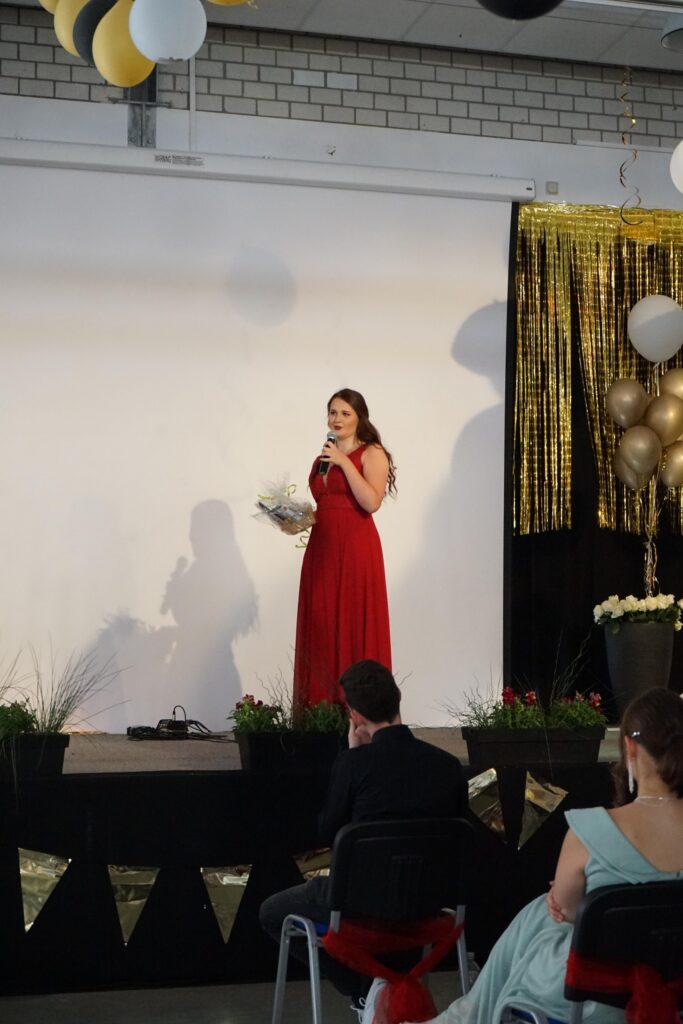 Eine Frau in rotem Kleid steht auf einer Bühne und spricht ins Mikrofon.