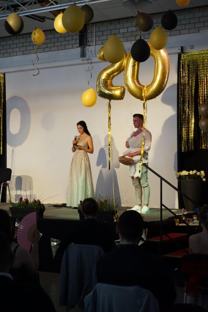 Eine Feier mit zwei Personen auf einer Bühne, umgeben von Dekoration in schwarz und Gold.