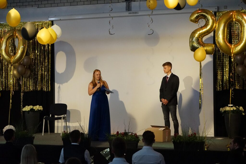 Veranstaltung mit dekorierten Luftballons und zwei Personen auf einer Bühne.
