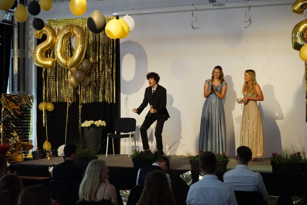 Zwei Frauen und ein Mann stehen auf einer Bühne mit Ballons und Dekoration.