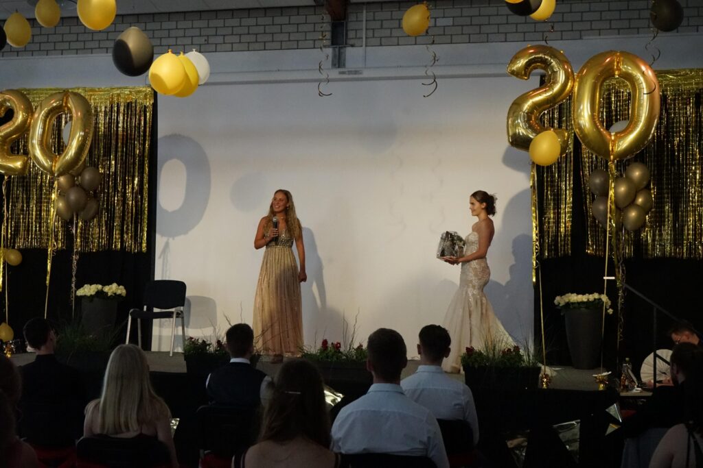 Zwei Frauen stehen auf einer Bühne vor einer festlichen Dekoration zum 20. Jubiläum.