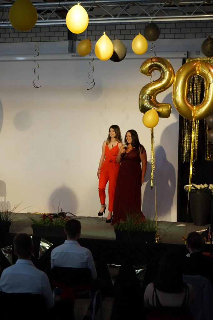 Zwei Frauen stehen auf einer Bühne mit goldenen Ballons und Dekoration.