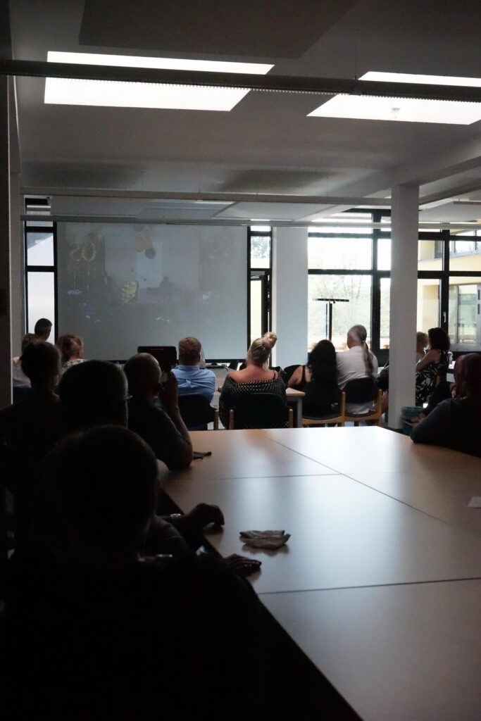 Gruppensitzung mit Präsentation in einem Seminarraum. Tische und Stühle sind sichtbar.