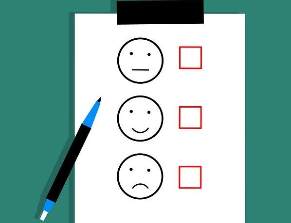 Umfragebogen mit Smileys und Kontrollkästchen, daneben ein blauer Stift.
