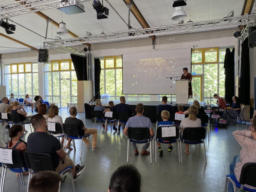 Ein Vortrag in einem Aula mit Sitzenden Zuhörern und einer Präsentation im Hintergrund.