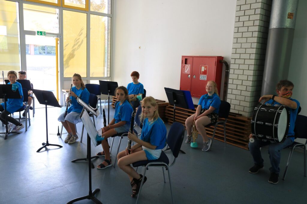 Schüler spielen in blauen T-Shirts Musikinstrumente in einem Probenraum.