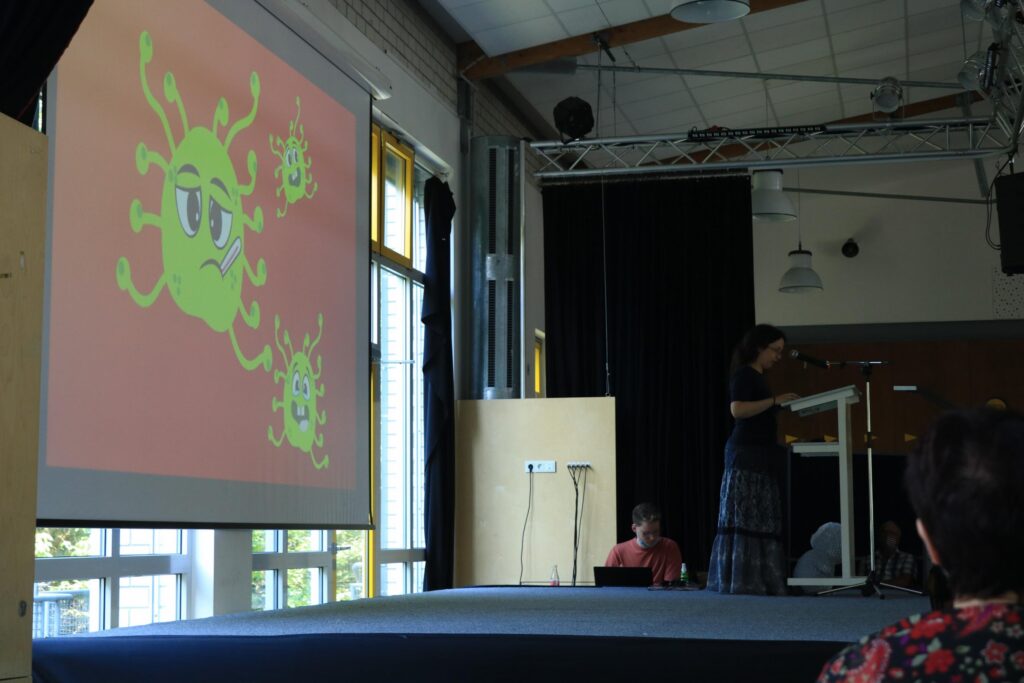 Schülerin präsentiert vor einem Bildschirm mit einem Comic-Virus.