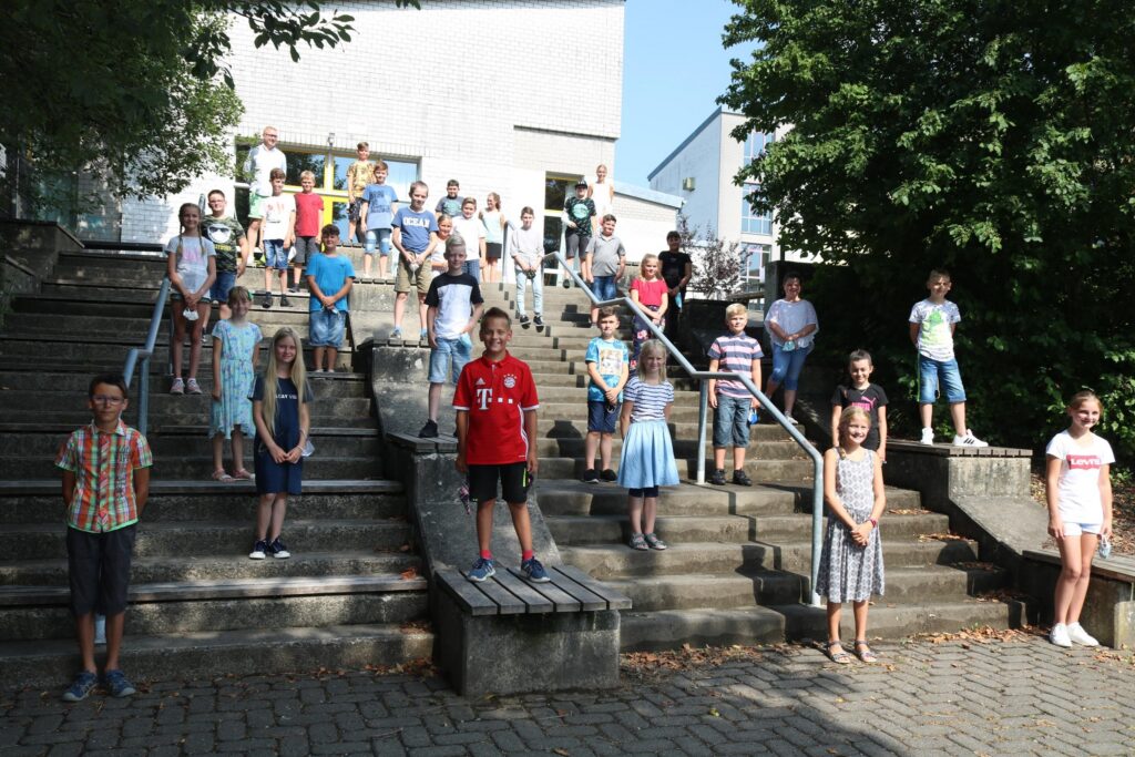 Schüler stehen auf Treppenstufen vor einem Schulgebäude.