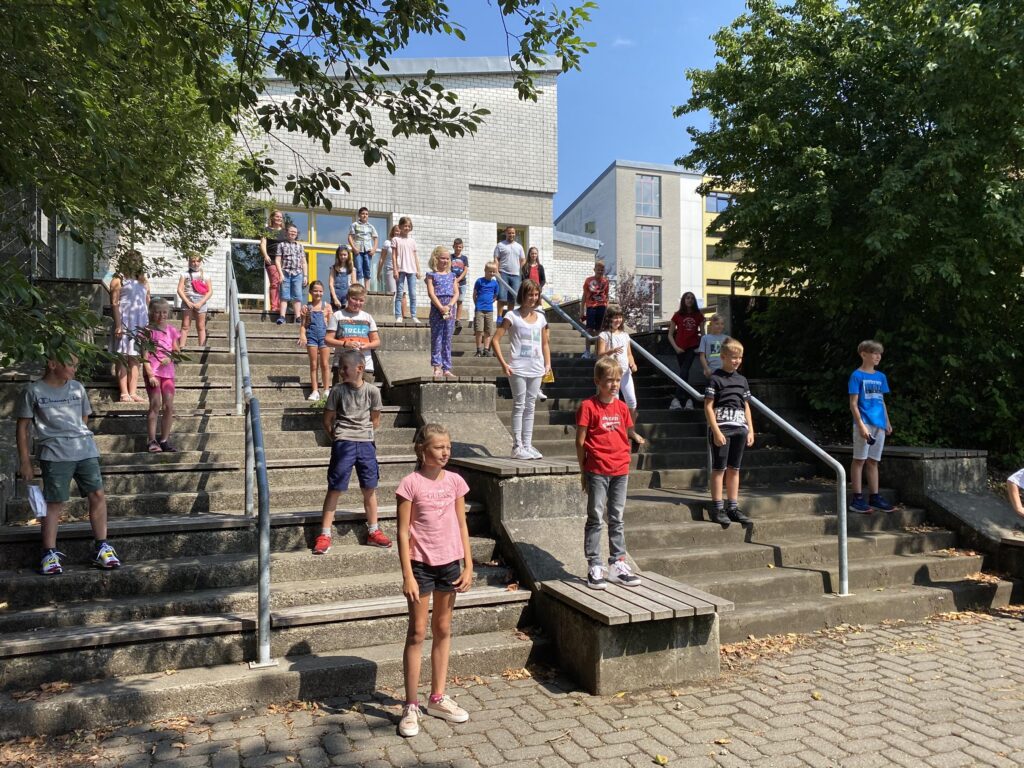 Schüler stehen auf einer Treppe vor der Schule an einem sonnigen Tag.