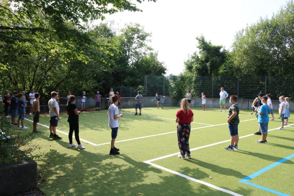 Schüler stehen an einem Sportplatz in Gruppen und warten auf Übungen.