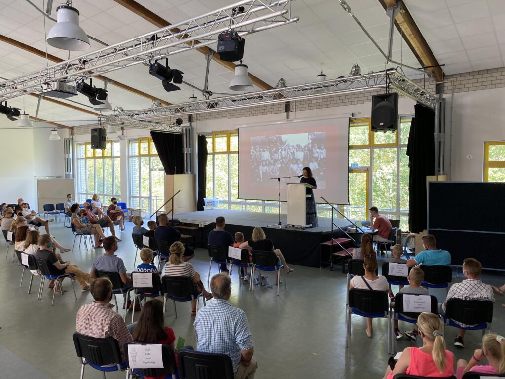Vortragssituation mit Publikum in einem großen Raum, Bühne im Hintergrund.