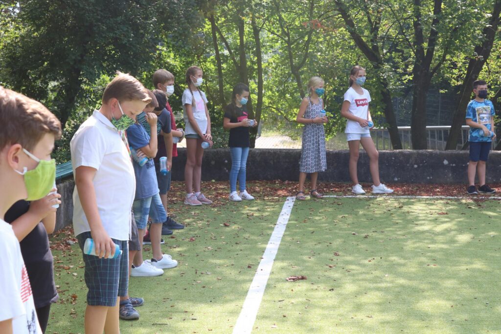 Schüler stehen mit Masken auf einem Sportplatz in einer Reihe.