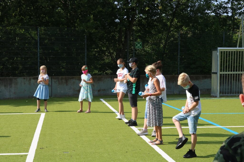 Schüler stehen auf einem Sportplatz und halten ihre Hände auf hüfthöhe.