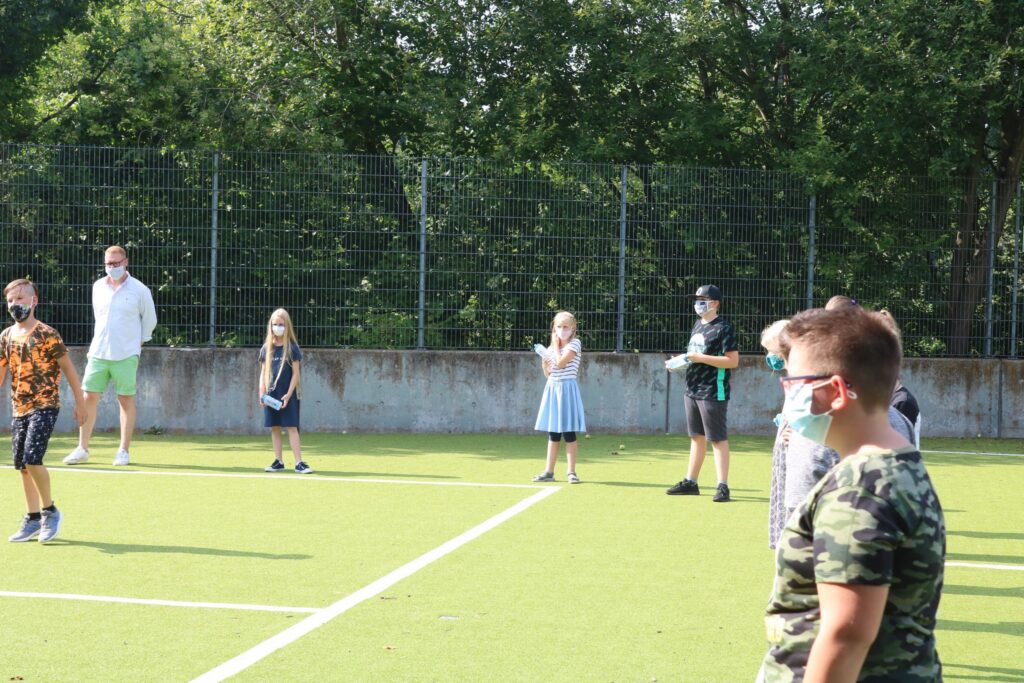 Kinder und Erwachsene stehen auf einem Sportplatz und tragen Masken.
