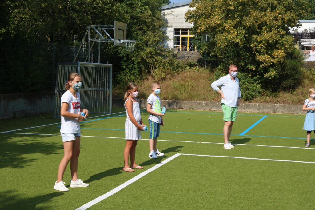 Kinder und Erwachsene stehen mit Masken auf einem Sportplatz.