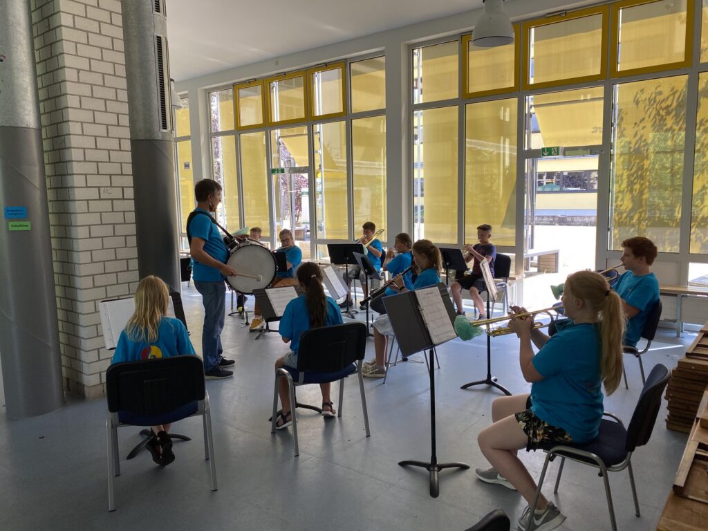 SchülerInnen mit Instrumenten proben in einem hellen Raum.