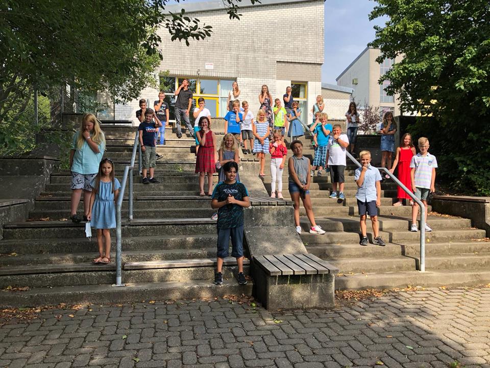 Schülerinnen und Schüler stehen auf Treppen vor einem Schulgebäude.