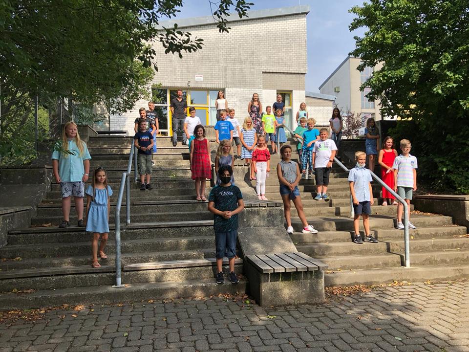 Schüler stehen auf Treppe vor Schulgebäude, einige posieren.