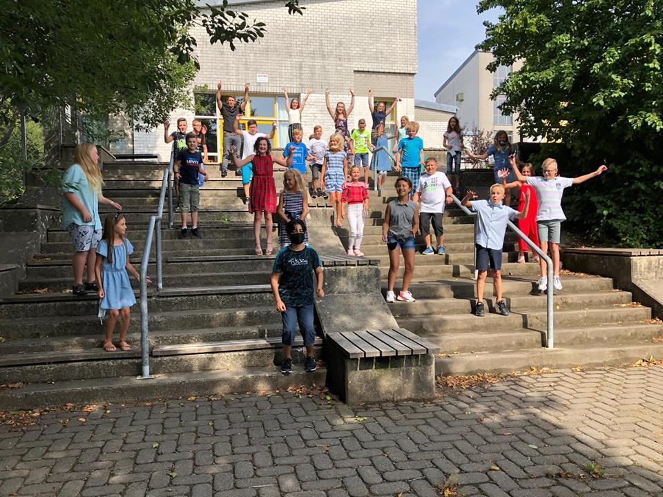 Schüler stehen auf Treppen im Freien und posieren fröhlich für ein Gruppenfoto.