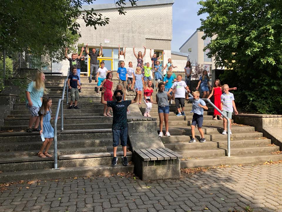 Gruppe von Schülern posiert auf Treppe vor Schulgebäude.