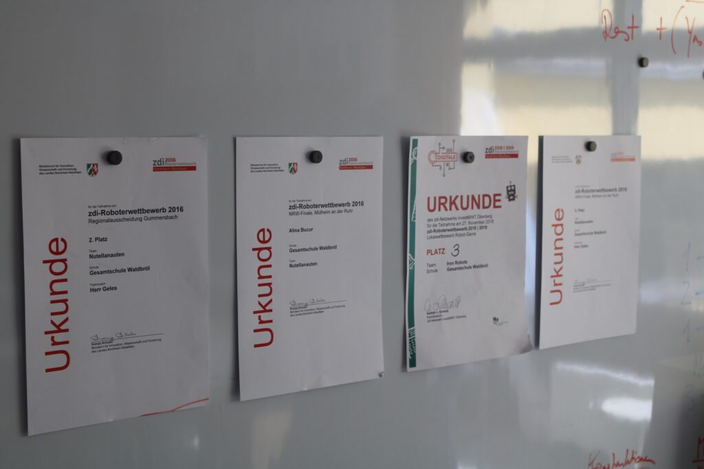 Zwei Urkunden und zwei Dokumente an einer Wandtafel.