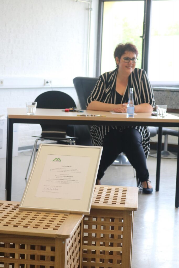 Eine Frau sitzt an einem Tisch mit einer Urkunde vor ihr.