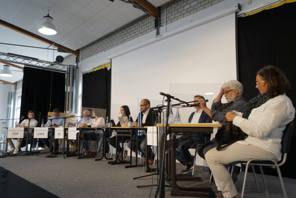 Eine Diskussionsrunde mit mehreren Personen an Tischen und Mikrofonen.