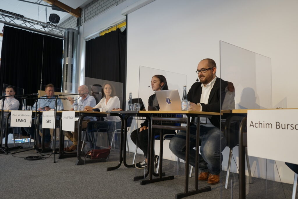 Podiumsdiskussion mit mehreren Teilnehmern und einem Moderator am Tisch.