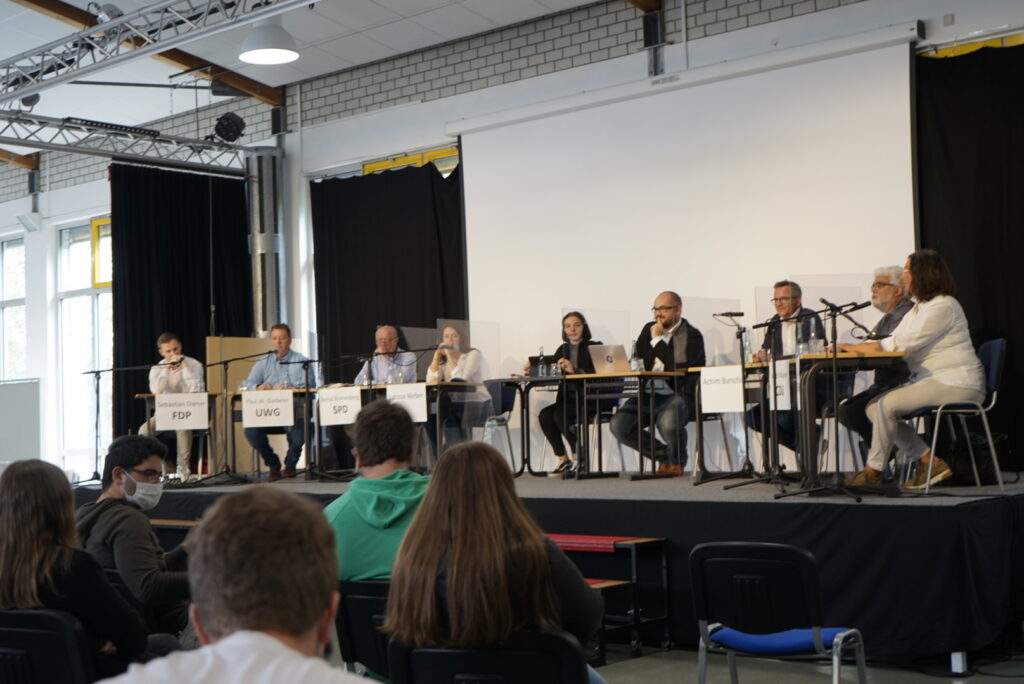 Podiumsdiskussion mit mehreren Sprechern auf der Bühne vor Publikum.