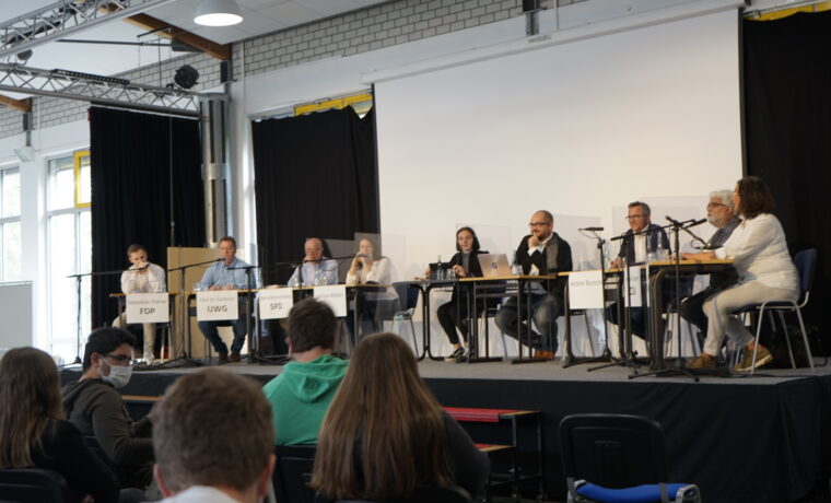 Podiumsdiskussion mit mehreren Sprechern auf der Bühne vor Publikum.