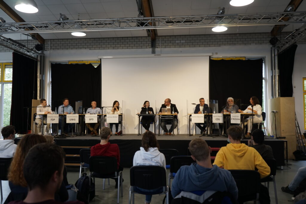 Podiumsdiskussion mit Sprechern auf der Bühne vor Publikum.