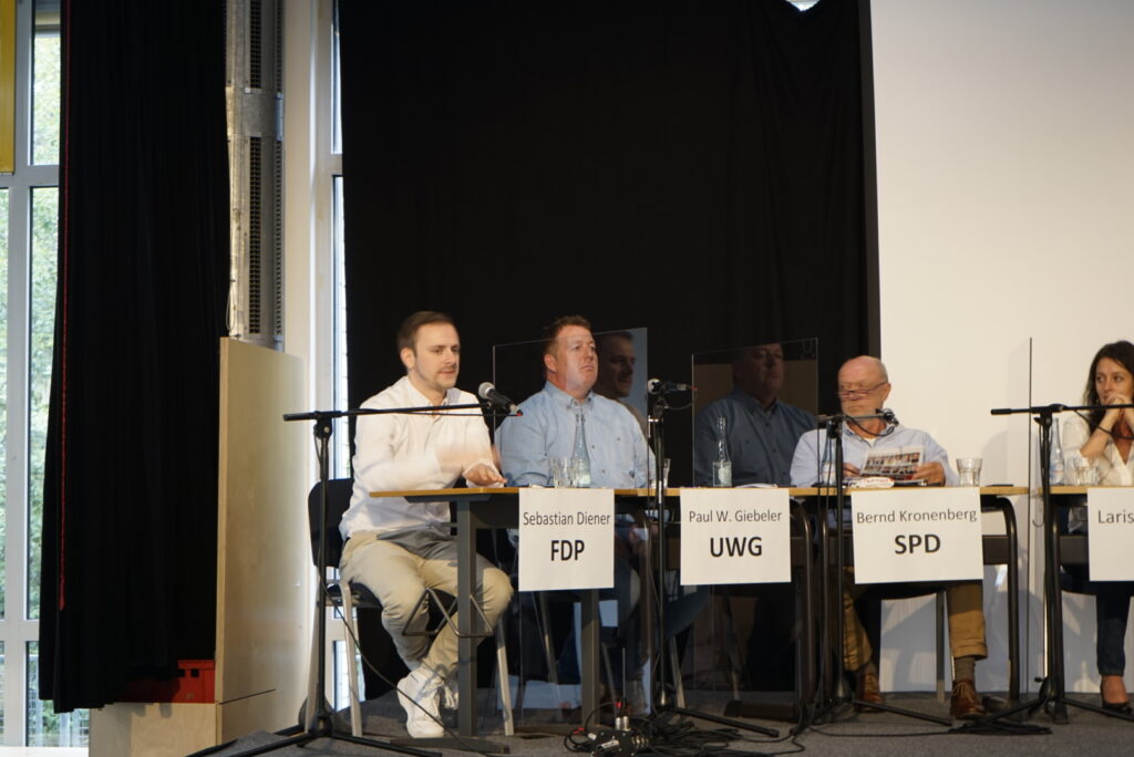 Podiumsdiskussion mit mehreren Rednern an Tischen.
