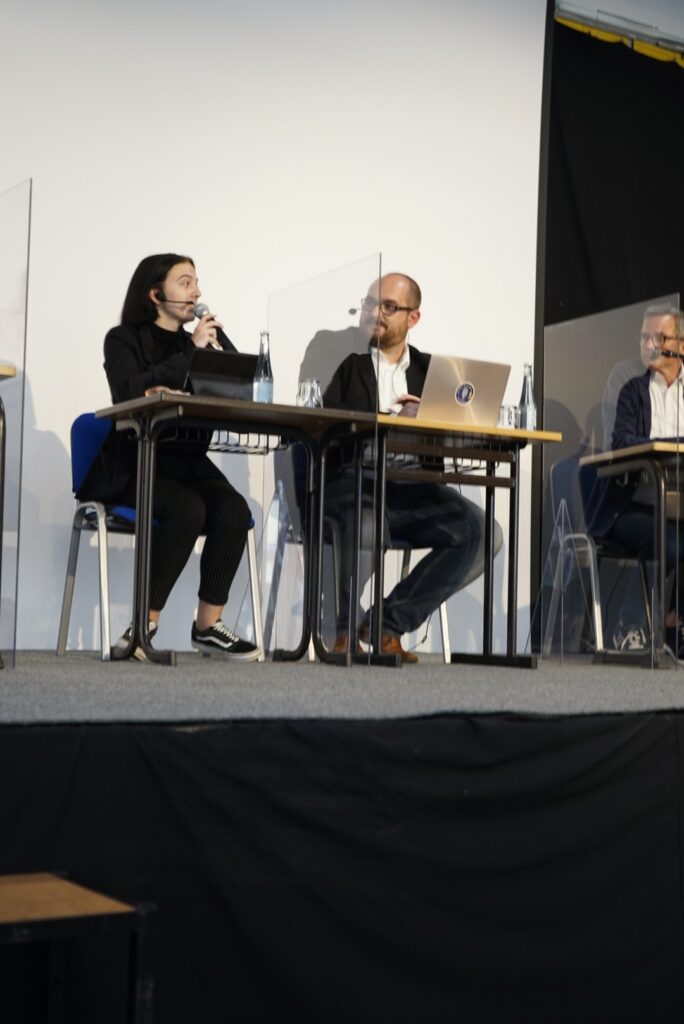 Podiumsdiskussion mit vier Personen an Tischen, die kommunizieren.