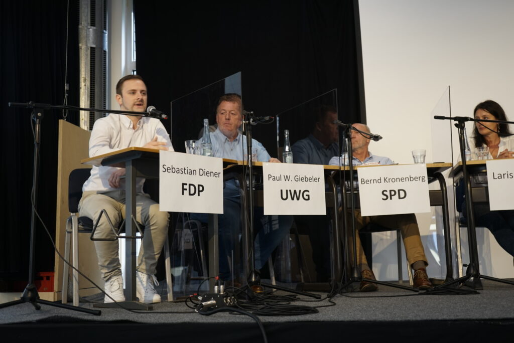 Podiumsdiskussion mit vier Rednern an Tischen und Mikrofonen.