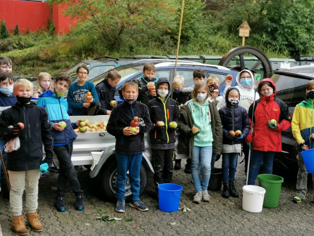 Schülerinnen und Schüler stehen gruppiert mit Äpfeln vor Autos und Eimern.