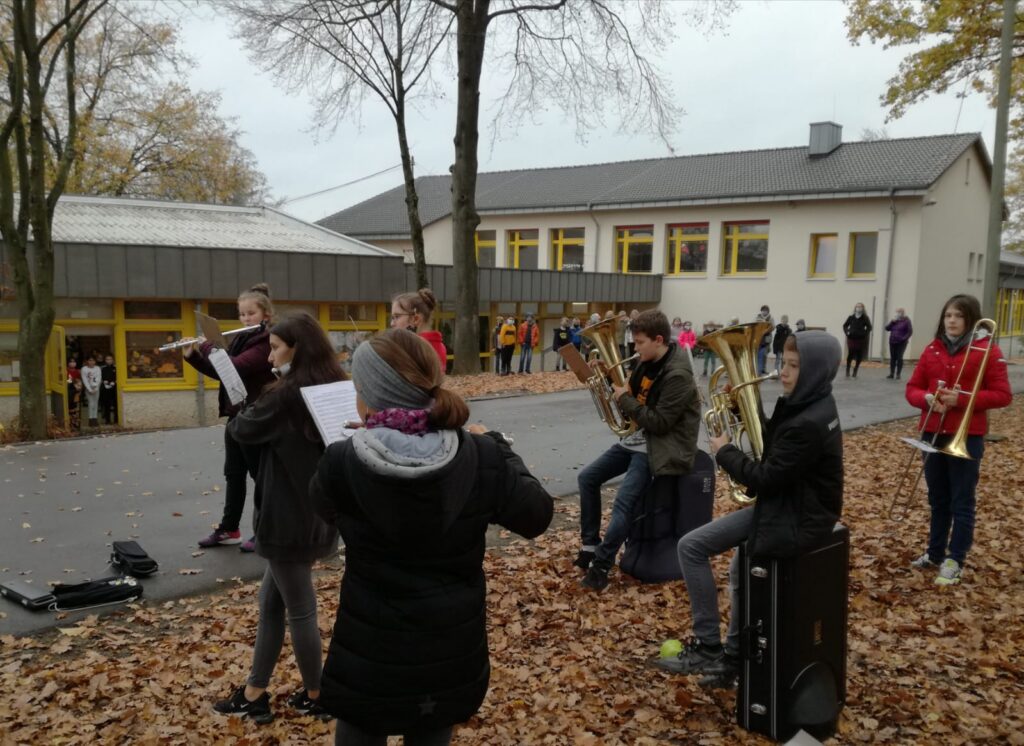 Schüler spielen Musik im Freien, umgeben von Bäumen und herbstlichen Blättern.