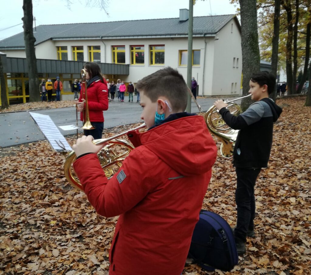 Zwei Kinder spielen Horn in einem herbstlichen Schulhof. Blätter liegen am Boden.