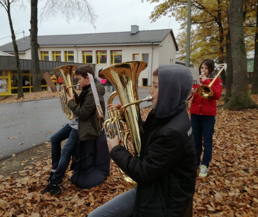Schüler spielen Blasinstrumente im Herbst auf einem Schulgelände.