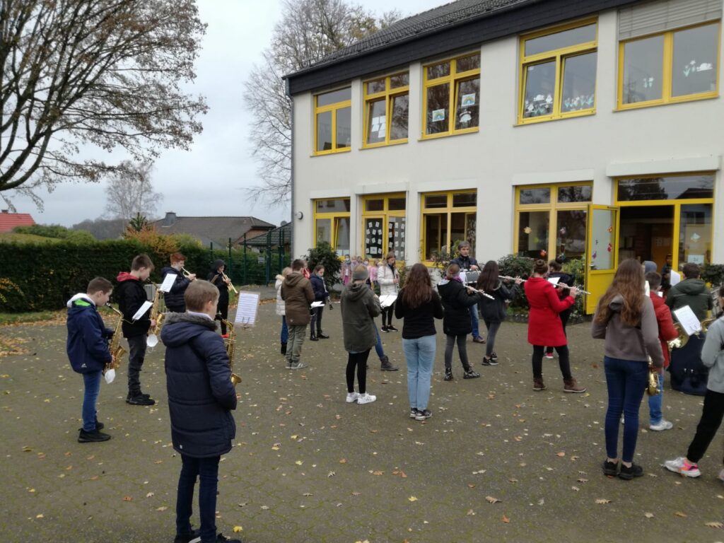 Schüler stehen in Gruppen draußen vor der Schule und halten Plakate.