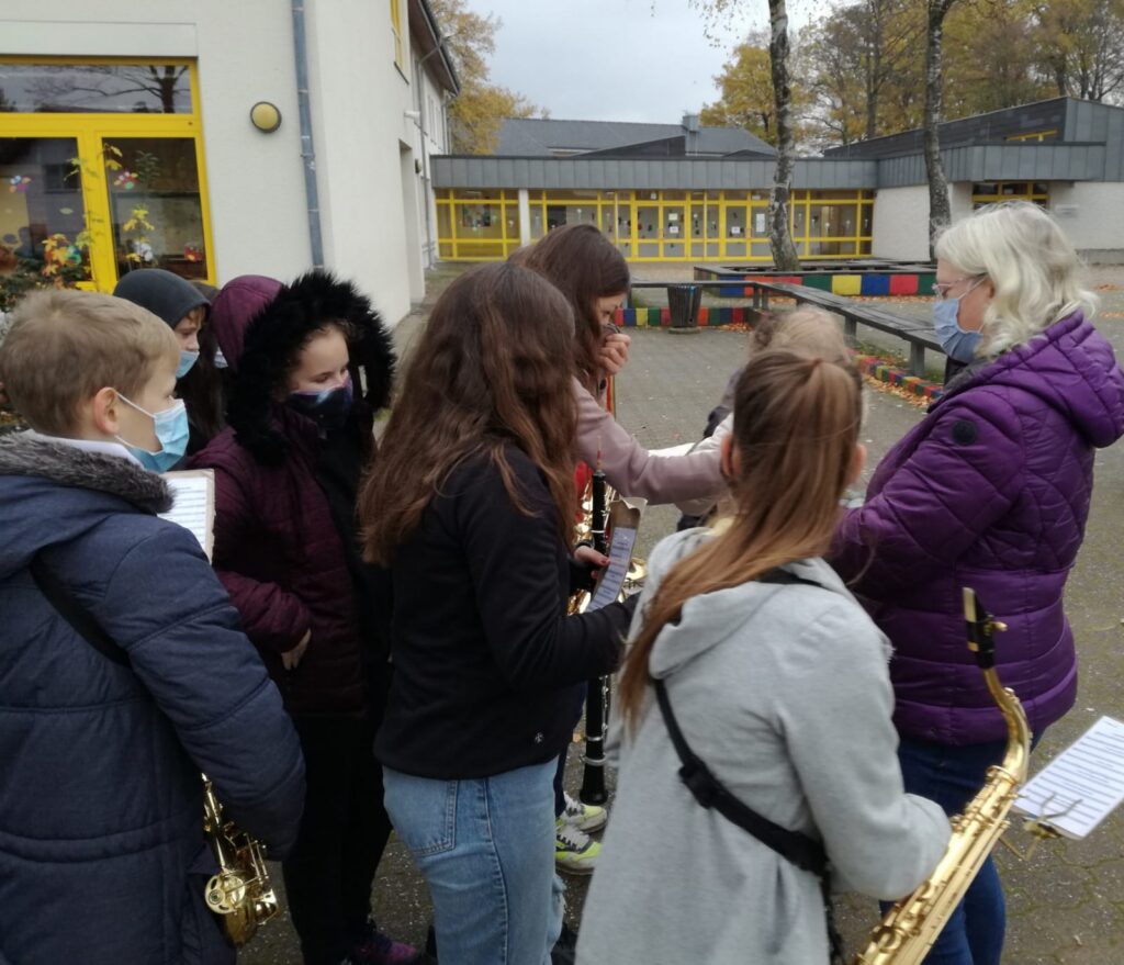 Schülerinnen und Schüler mit Blasinstrumenten stehen im Freien und proben.