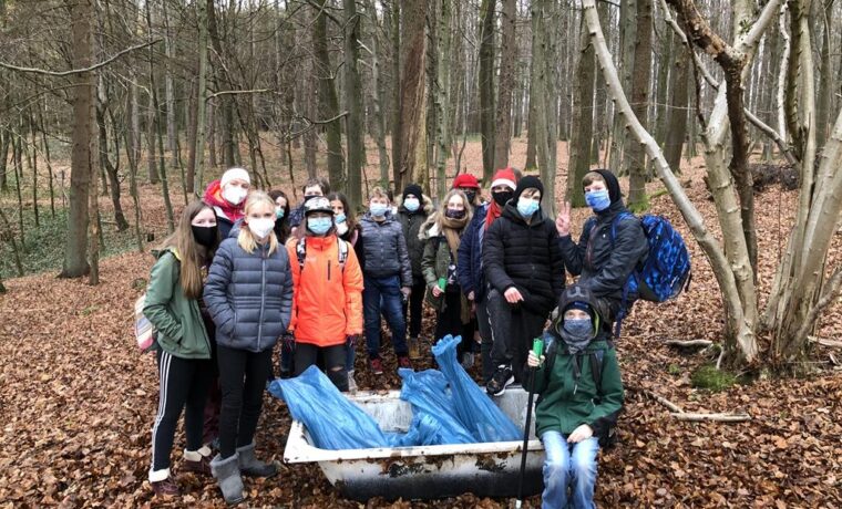 Gruppe von Schülern im Wald, umgeben von Laub, mit einem Karren und Müllsäcken.