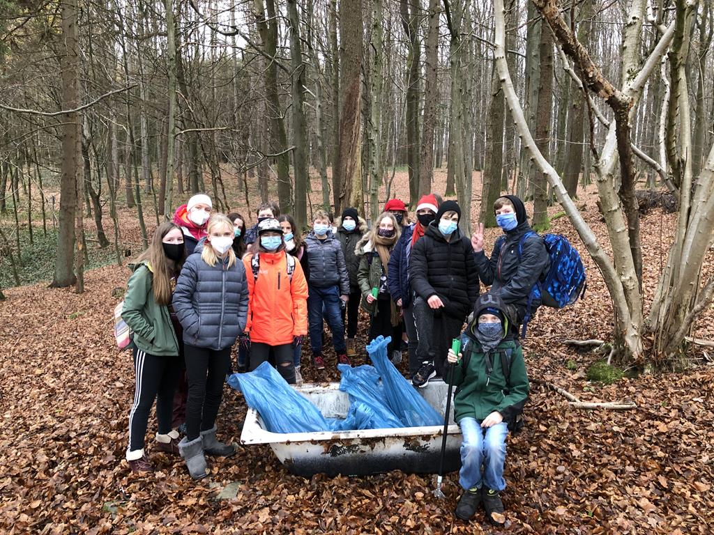 Gruppe von Schülern im Wald, umgeben von Laub, mit einem Karren und Müllsäcken.