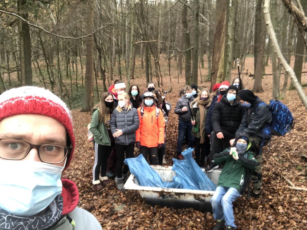 Gruppe von Personen in einem Wald, einige mit Masken, bei einer Umweltaktion.