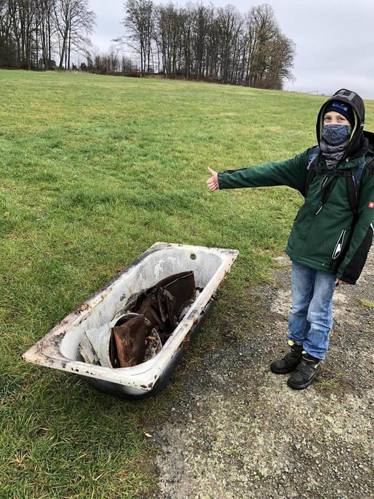 Junge steht neben einer alten Badewanne auf einer Wiese.