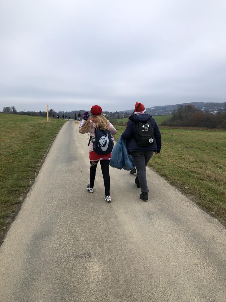 Zwei Personen gehen einen Weg entlang, tragen Mützen und Rucksäcke.