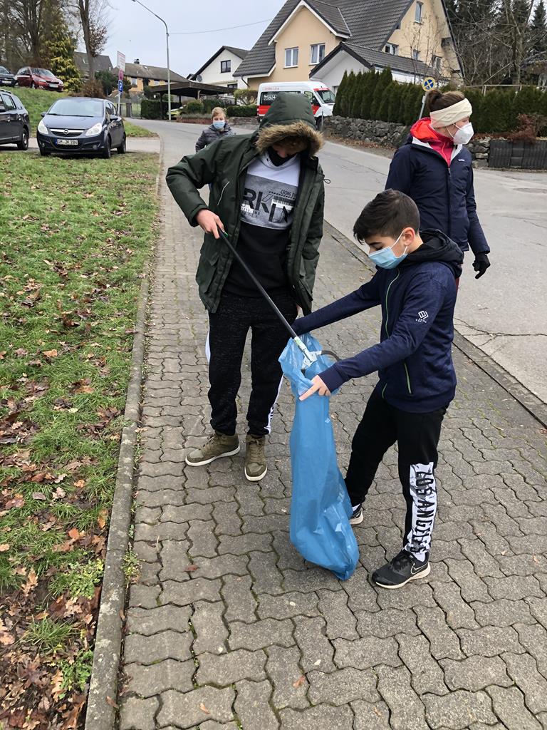 Zwei Kinder sammeln Müll auf der Straße in einer Wohngegend.