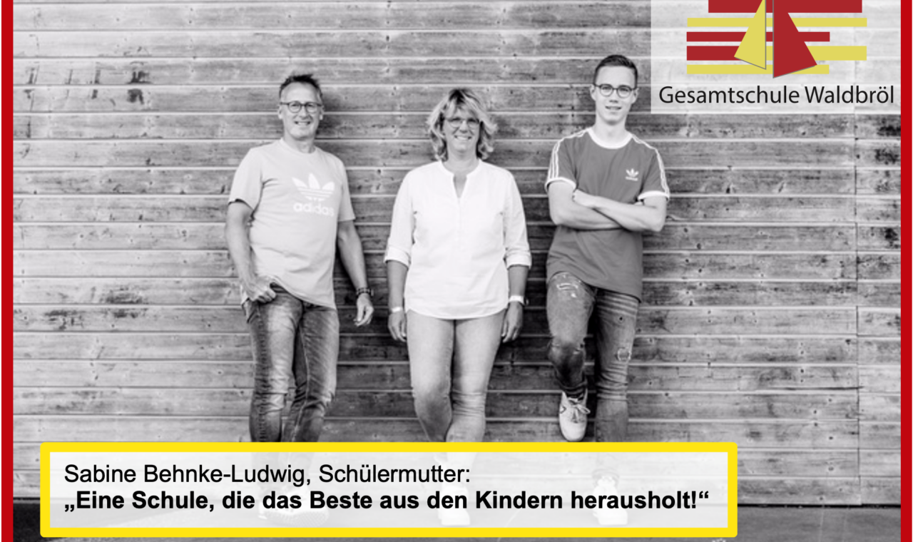 Drei Personen stehen vor einer Holzwand, mit einem Zitat zur Schule.